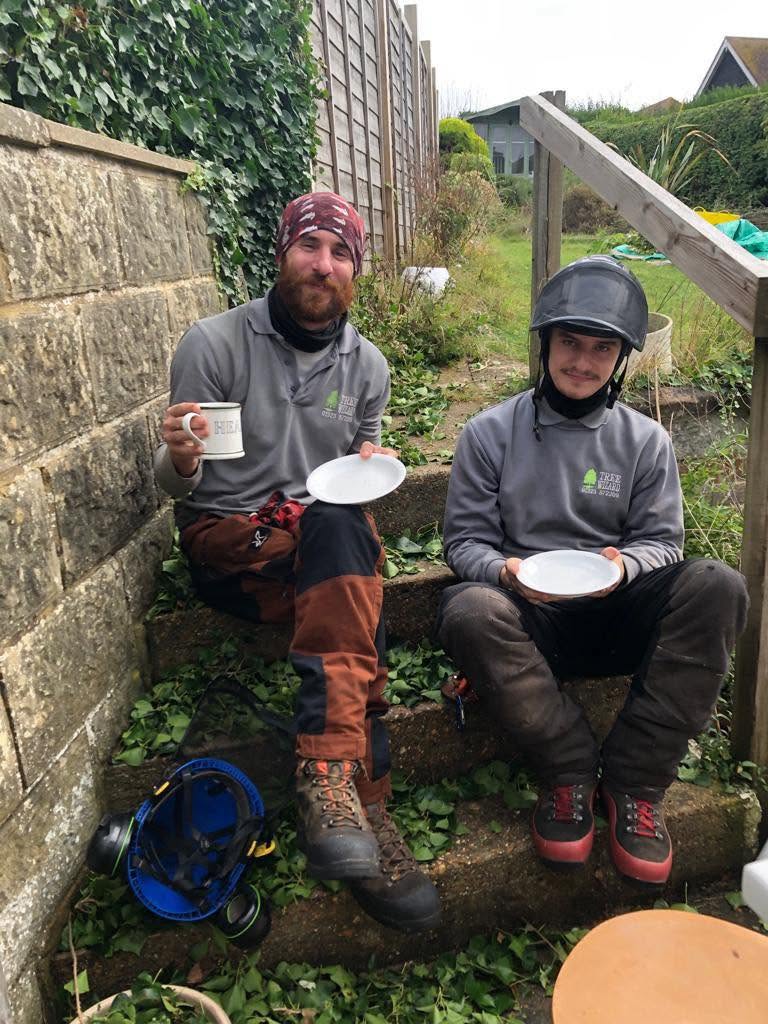 Two of the Tree Wizard crew in their branded tops, taking a tea break on garden steps